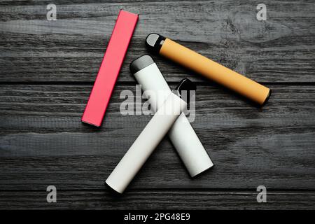 Différentes cigarettes électroniques jetables sur table en bois noir, plat. Alternative fumeurs Banque D'Images