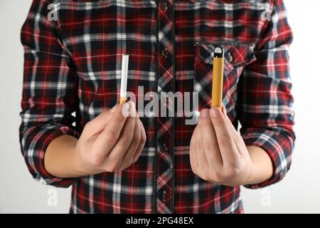 Homme avec une cigarette et un appareil de vapotage sur fond clair, gros plan. Alternative fumeurs Banque D'Images