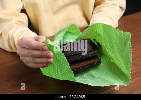 Femme emballant des tranches de pain de seigle dans la cire d'abeille nourriture envelopper à table en bois, gros plan Banque D'Images