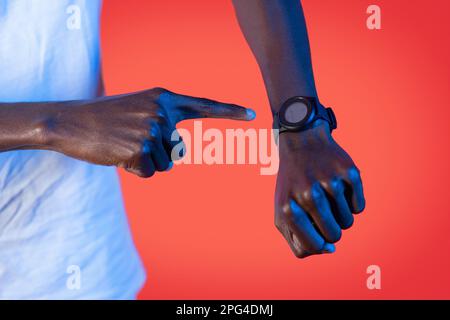 Homme noir au néon avec montre intelligente à portée de main, arrière-plan rouge Banque D'Images