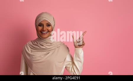 Offre agréable. Une femme islamique souriante dans le hijab pointant de côté sur Copy Space Banque D'Images