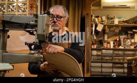 vue en face d'un artisan en cuir assis tout en coudre le dos d'une chaise faite par lui dans l'atelier, rome, italie Banque D'Images