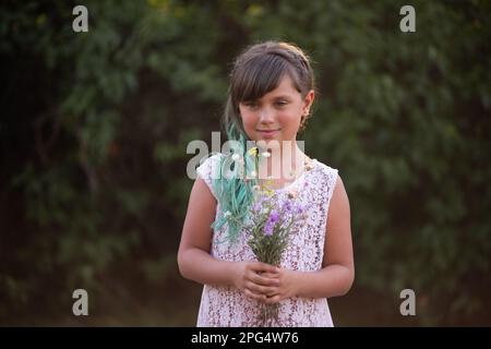 Fille à cheveux verts tient le bouquet de fleurs sauvages sur fond botanique, regarde dans l'appareil photo. Cadeau naturel doux pour la mère. Génération Z dans bri Banque D'Images