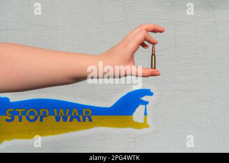 Cartouche de fusil en main. Une ombre jaune-bleu est formée sur le mur avec l'inscription - STOP WAR. Le concept de soutien militaire à l'Ukraine Banque D'Images