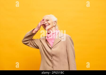 Femme âgée gaie en tenue décontractée élégante couvrant la moitié du visage à la main et riant à quelque chose de drôle sur fond jaune Banque D'Images