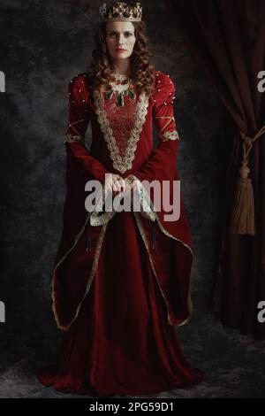 reine médiévale en robe rouge avec couronne sur fond gris foncé. Banque D'Images