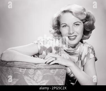 1940S PORTRAIT D'UNE FEMME SOURIANTE REGARDANT L'APPAREIL PHOTO PORTANT UN COLLIER EN PERLES ET UN ANNEAU DE MARIAGE APPUYÉ SUR LE BRAS DE LA CHAISE REMBOURRÉE - G628 HAR001 EXPRESSIONS DU SEA B&W CONTACT VISUEL FOYER DOMESTIQUES FEMMES TÊTE ET ÉPAULES GAIES ET SUR LES FEMMES AU FOYER SOURIRES CURIEUX JOYEUSE INTÉRESSÉE MOYENNE-ADULTE MOYENNE-ADULTE BAGUE DE MARIAGE NOIR ET BLANC RACE BLANCHE HAR001 OLD FASHIED Banque D'Images