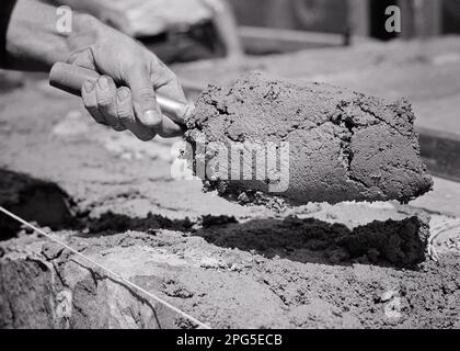 1950S MAIN D'UN HOMME TENANT UNE TRUELLE PLEINE DE MORTIER CIMENT DE CONSTRUCTION D'UN MUR DE PIERRE OU DE CONSTRUCTION FONDATION - S1532 HAR001 HARS CONNEXION CONCEPTUELLE MAÇONNERIE LIANT EMPLOYÉ DE PIERRE SYMBOLIQUE CONCEPTS COMMERCIAUX MAINS NOIR ET BLANC SEULEMENT HAR001 JOINDRE TRAVAILLER REPRÉSENTATION À L'ANCIENNE Banque D'Images