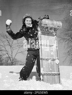 1940S 1950S BRUNETTE SOURIANTE FEMME JETANT UN BOULE DE NEIGE SE CACHANT DERRIÈRE UN TOBOGGAN EN BOIS - W1793 HAR001 HARS CACHANT DES TRAÎNEAUX RURAUX QUI TRAÎNAIENT À LA MAISON VIE COPIE ESPACE FEMMES PERSONNES CONFIANCE NEIGE B&W HIVER OEIL CONTACT BRUNETTE BONHEUR LUGE GAI GAIETÉ LOISIRS PROTECTION EXCITATION RÉCRÉATION DIRECTION SOURIT CONCEPTUEL JOYEUSE TOBOGGANING HIVER NEIGE COMBINAISON BOULE DE NEIGE LUTTE LAINE VESTE JEUNE ADULTE FEMME NOIR ET BLANC RACE BLANCHE HAR001 DÉMODÉE Banque D'Images