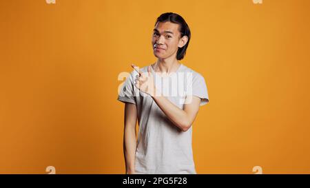Personne asiatique pointant latéralement avec les index, regardant les côtés gauche ou droit et étant confiant. Jeune homme modèle indiquant des directions à part en studio, posant avec confiance sur la caméra. Banque D'Images