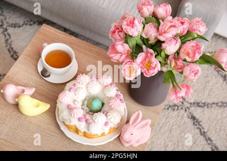 Gâteau de Pâques, lapin, cailles en porcelaine et vase avec fleurs de tulipe sur table dans le salon Banque D'Images