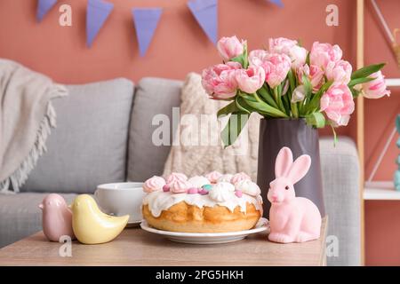 Gâteau de Pâques, lapin, cailles en porcelaine et vase avec fleurs de tulipe sur table dans le salon Banque D'Images