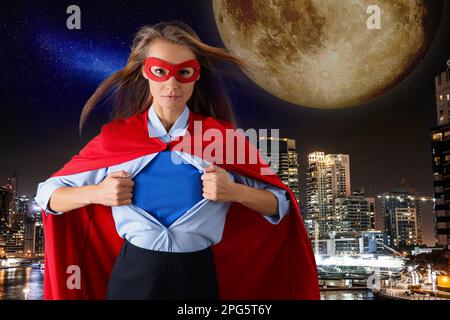 Femme d'affaires confiante portant un costume de super-héros sous le costume et un magnifique paysage urbain en arrière-plan la nuit Banque D'Images