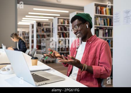 Étudiant noir souriant ou indépendant dans un casque à l'aide d'un ordinateur portable regardant l'écran faire des appels vidéo. Banque D'Images
