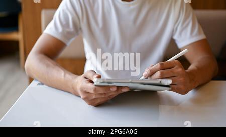 Vue rapprochée d'un jeune homme travaillant dans un café tout en utilisant une tablette numérique. dessin, esquisse, écriture Banque D'Images