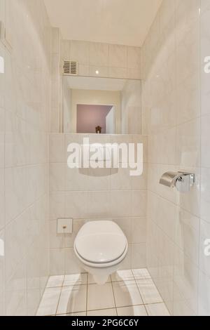 une toilette blanche dans une salle de bains avec sol carrelé et miroir mural au-dessus des toilettes est une image de la réflexion d'une femme Banque D'Images