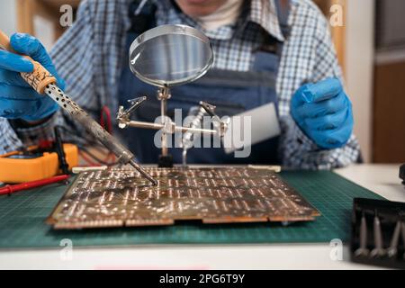 Réparation d'ordinateurs ou de composants électroniques par un contremaître dans un atelier. Soudage manuel des cartes électroniques. Service. Fermez les mains. Banque D'Images