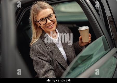 Femme d'affaires attirante entrepreneur portant des lunettes avec le café à emporter sortant de la voiture Banque D'Images