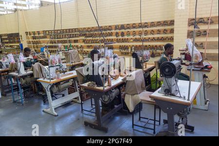 Homme portant des lunettes dans une usine de chaussures en cuir utilisant une machine à coudre pour créer des empeignes en cuir Banque D'Images