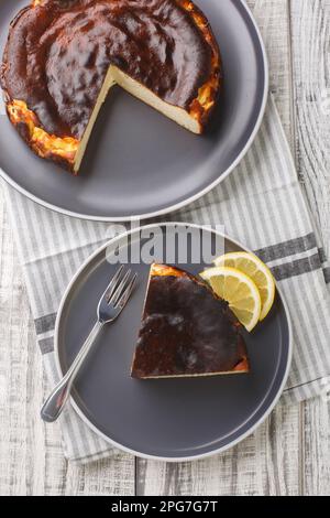 Émincé de cheesecake basque crémeux et tendre avec des quartiers de citron sur une assiette sur la table. Vue verticale du dessus Banque D'Images