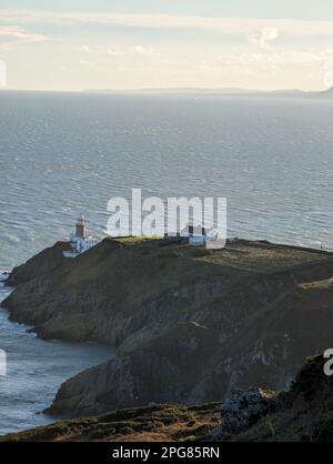 Un phare majestueux se dresse au sommet d'une colline rocheuse surplombant un plan d'eau tranquille Banque D'Images