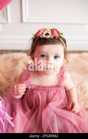 Une petite fille habillée dans une tenue rose assise sur un tapis flou dans un environnement confortable Banque D'Images