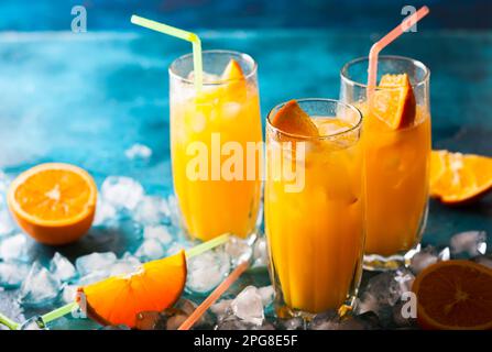 Jus d'orange frais dans des verres, des cubes de glace et une tranche de fruits sur une table bleue. Boisson saine de vitamine. Banque D'Images