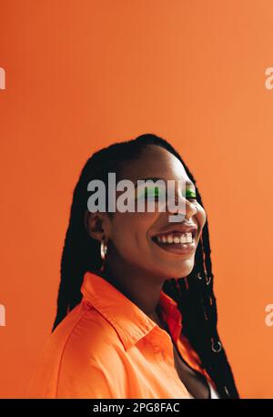 Joyeuse femme africaine au maquillage et au visage piercings souriant avec ses yeux fermés. Jeune femme heureuse avec des dreadlocks debout contre un studio Backgr Banque D'Images