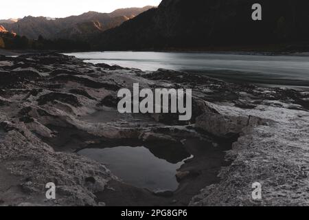 Les renfoncements dans une pierre de différentes roches sont remplis d'eau sur la rive de la rivière de montagne Katun près d'un rocher dans Altai au coucher du soleil à l'ombre dedans Banque D'Images