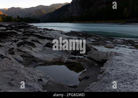 Les renfoncements dans une pierre de différentes roches sont remplis d'eau avec réflexion sur la rive de la rivière de montagne Katun près d'un rocher dans Altai au coucher du soleil Banque D'Images