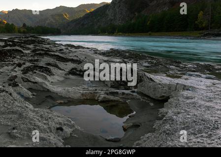 Les renfoncements dans une pierre de différentes roches sont remplis d'eau sur la rive de la rivière de montagne Katun près d'un rocher dans Altai au coucher du soleil à l'ombre dedans Banque D'Images