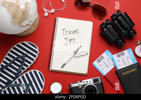 Composition de pose à plat avec conseils de voyage de phrase écrits dans un carnet, passeports, billets et jumelles sur fond rouge Banque D'Images