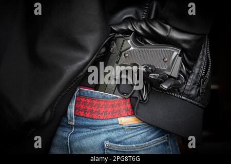 Un homme, un policier ou un voleur, un gangster dissimule son arme derrière son dos. Le tireur tire une arme à feu sous une veste en cuir noir. Banque D'Images