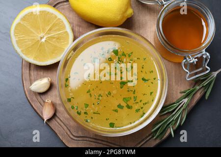 Bol avec sauce au citron et ingrédients sur table sombre, vue de dessus. Délicieuse vinaigrette Banque D'Images
