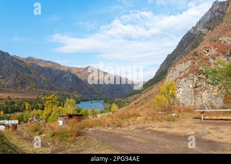 Un banc et des maisons de vacances sur une colline au milieu des montagnes près de la rivière en Altai en Sibérie pendant la journée. Banque D'Images