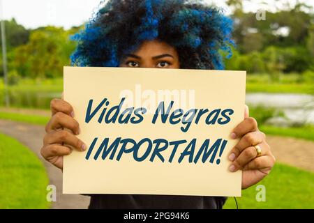 Goiania, Goias, Brésil – 18 mars 2023: Une jeune femme, avec des cheveux teints en bleu, son visage caché derrière un signe avec le texte: 'Les vies noires comptent'. Banque D'Images