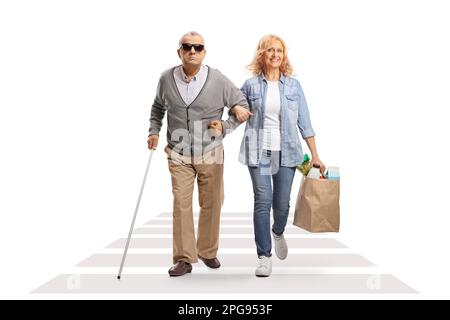 Femme aidant un homme aveugle senior avec des sacs d'épicerie traversant une rue isolée sur fond blanc Banque D'Images