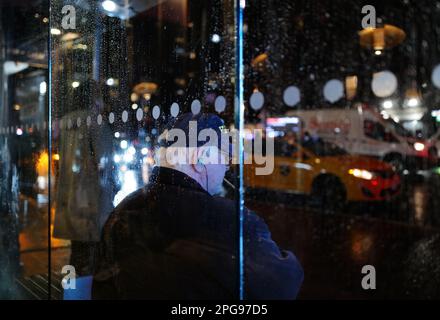 Homme assis à un arrêt de bus lors d'une nuit de pluie à New York Banque D'Images