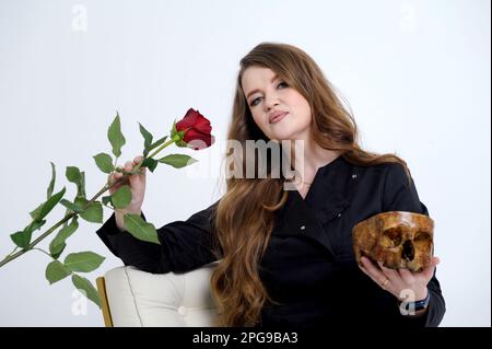 Forte femme sérieuse dans ses mains avec une rose et un crâne humain est assis sur un fond blanc dans les vêtements noirs médecine pouvoir amour occasions perdues vie et mort insidieuse femme cruelle vamp Banque D'Images