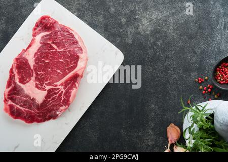 Steak de ribeye frais cru ou steak de Rib-Eye. Viande crue fraîche marbrée Ribeye Black Angus et assaisonnements poivre, romarin, thym et sel sur le vieux rusti en bois Banque D'Images