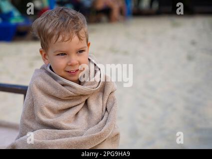 Le bébé, enveloppé d'une serviette, se réchauffe sur un transat au bord de la mer. Bébé en prévision du bain Banque D'Images