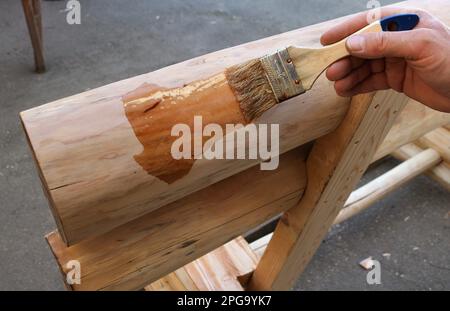 une main applique une couche de vernis avec un pinceau sur un fragment d'un banc en bois fait à la main, vernis transparent d'un produit en bois massif Banque D'Images