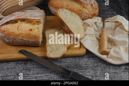 Pain croustillant tranché sur une planche à découper en bois avec un couteau à pain et une partition de pain et un panier de banneton vue latérale Banque D'Images