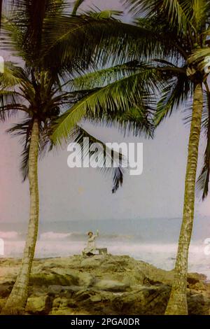 Une dame européenne assise sur des rochers près de l'océan Atlantique à Accra, Ghana vers 1960 Banque D'Images