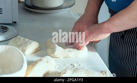 Un chef cuisinier fait du pain maison sur une table blanche. Chef étirant et pliant la pâte à pain sur une table blanche avec vue latérale sur la farine saupoudrée. Banque D'Images