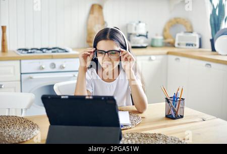 Jolie fille 12s porter des écouteurs et des lunettes faire la tâche, étudier en ligne, éprouve des problèmes de vision, des calmars, avoir la vue tombe, problèmes de santé Banque D'Images