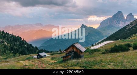 Paysage alpin paisible des Alpes italiennes, lumière dorée orange chaude du soleil du matin illumine les maisons en bois pittoresques et les prairies verdoyantes o Banque D'Images