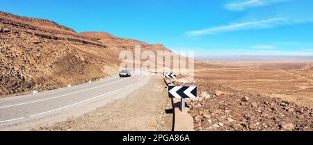 Courbe sur route asphaltée, petites montagnes de l'Atlas et buissons bas des deux côtés, ciel clair au-dessus - paysage typique dans le sud du Maroc Banque D'Images