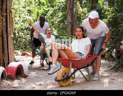 Les hommes conduisent leurs filles dans les brouettes de jardin. Funny parc d'amusement park Banque D'Images