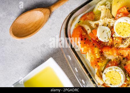 Gomes de sa morue rôtie dans de l'huile d'olive avec tomates, poivrons, oignons, œufs durs et origan. Dans un plat rectangulaire en verre. Détail bois sp Banque D'Images